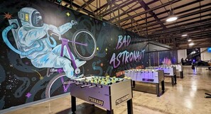 A space-themed room with foosball tables and a mural of an astronaut.