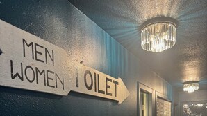 Un pasillo con un cartel direccional que indica 'MEN WOMEN TOILET' y una araña.