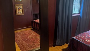Una habitación con un espejo grande, una cama con edredón estampado, piso de madera y una ventana con cortinas.