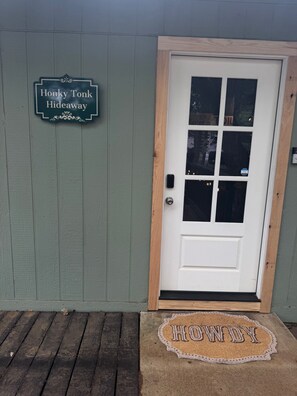Eine weiße Tür mit Holzrahmen, eine grüne Wand und ein Schild mit der Aufschrift 'Honky Tonk Hideaway'.