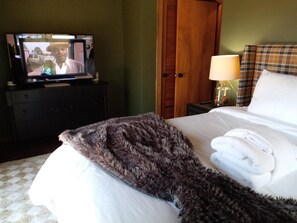 Una habitación de hotel con una cama, un televisor en una cómoda, una lámpara y un armario de madera.