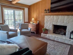 A cozy living room with a fireplace, wooden walls, a comfortable sofa, and a dining area visible through a glass door. - Adorable comfort on 2 acres close to hiking trails and scenic mountain drives (Mars Hill)