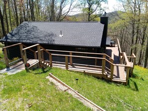 Una cabaña con techo negro, terraza de madera y zona cercada.