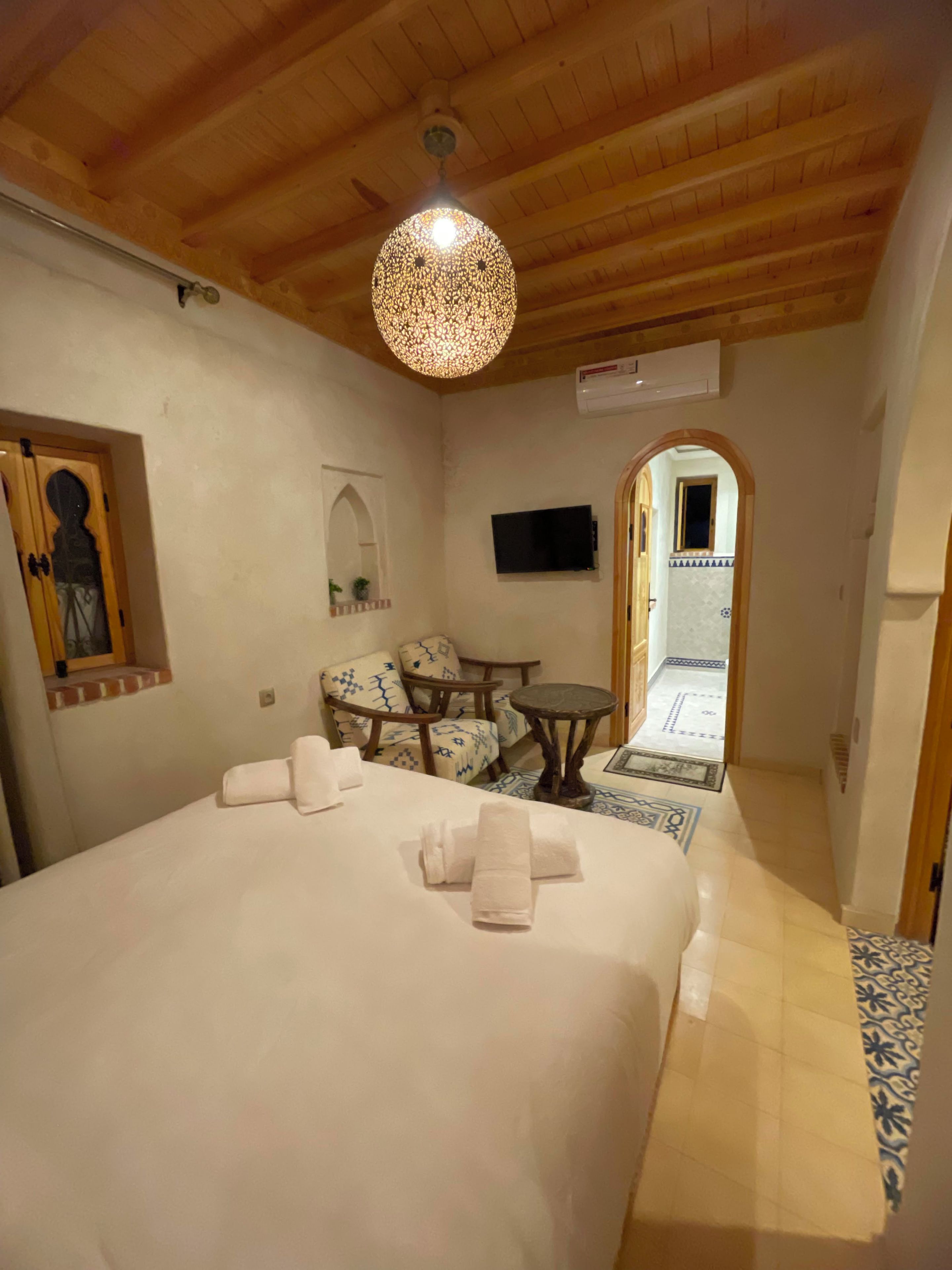Habitación de hotel con una cama grande, una mesita, dos sillas, un televisor y techo de madera.