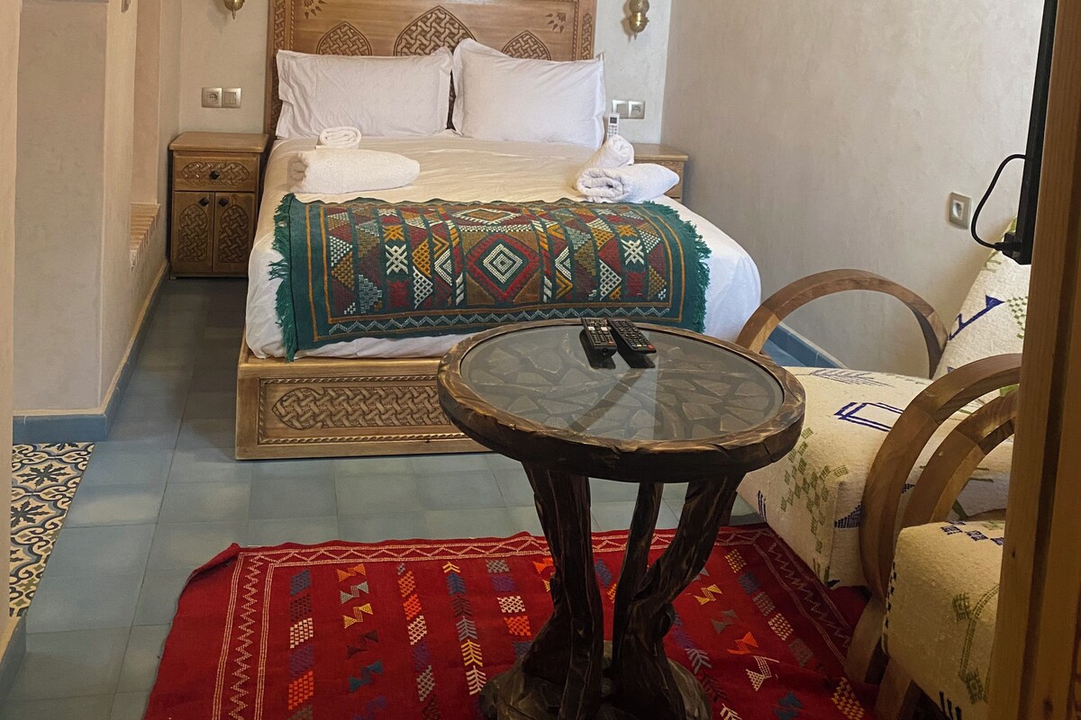 Un dormitorio con una cama de madera, una mesa redonda y una alfombra roja.