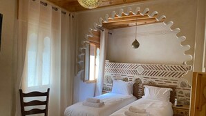 A bedroom with two beds, a wooden chair, a nightstand, and a decorative ceiling.