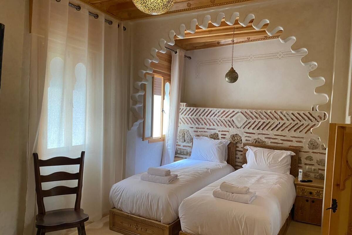 A bedroom with two beds, a wooden chair, a nightstand, and a decorative ceiling.