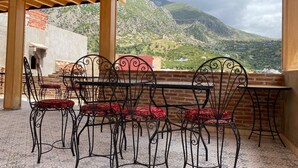 A covered outdoor seating area with metal chairs and a table, overlooking a mountainous landscape.