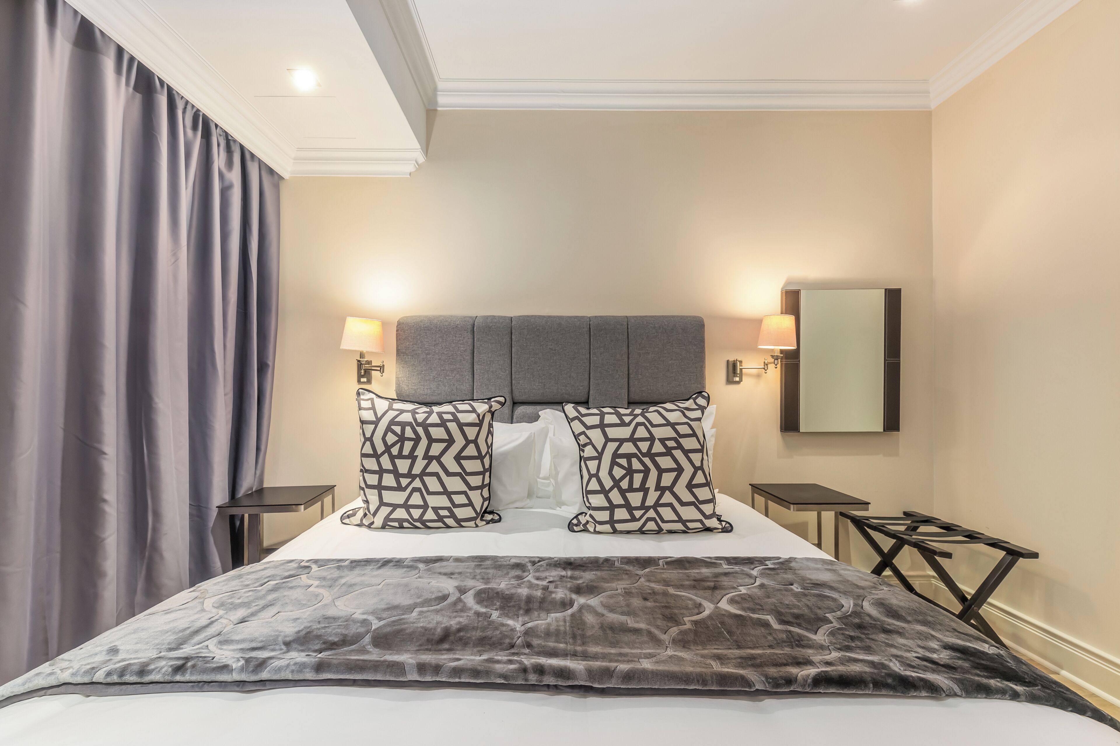 A hotel room with a large bed, two bedside tables, a headboard, and a mirror on the wall.