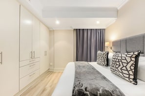 Ein Schlafzimmer mit Bett, Kissen, einem Nachttisch, einem Kleiderschrank und einem Fenster mit Vorhängen.