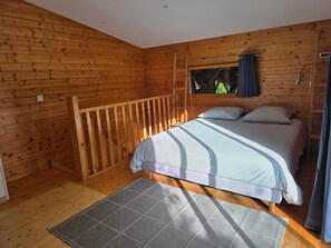 Une chambre dans une cabane en bois, avec un lit, une fenêtre avec des rideaux, une échelle et un plancher en bois.