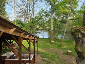 Un pavillon en bois, doté de bancs et de tables, entouré d’arbres et bordé par un lac.