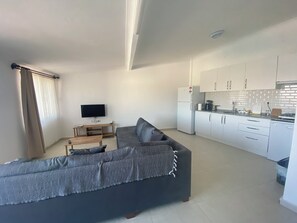A modern living room with a sofa, a TV, and a kitchen area with cabinets and appliances. - Stunning Waterfront Holiday at Datça Marina (Muğla)