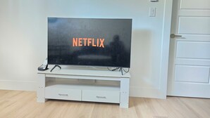 Un téléviseur posé sur un meuble blanc, avec un panneau indiquant « NETFLIX », une porte et un interrupteur sur le mur.