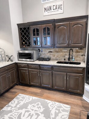 A kitchen with dark wooden cabinets, a microwave, a sink, and a patterned rug.