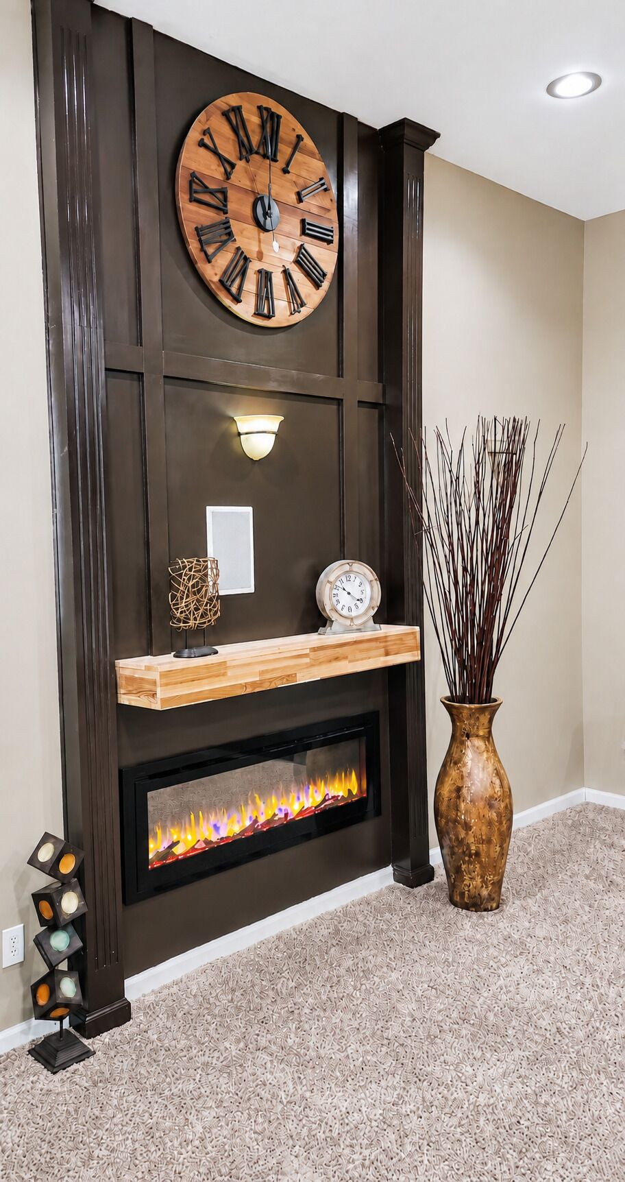A fireplace with a modern design, a large wooden clock, and a vase with decorative branches.