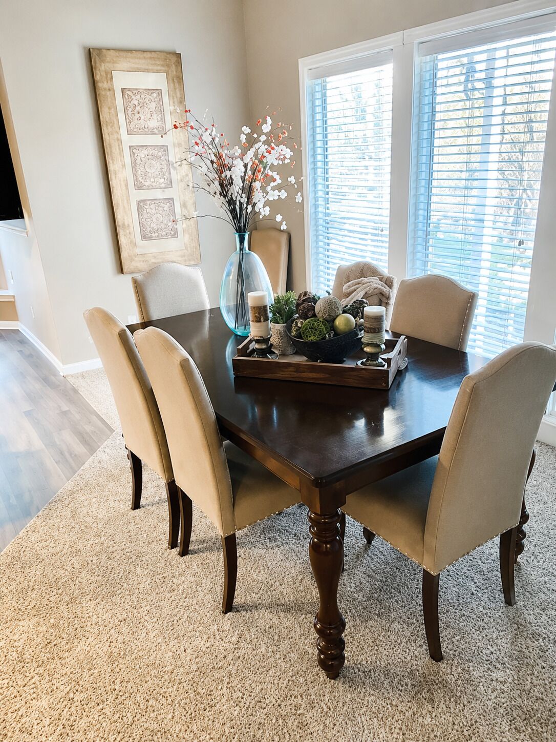 A dining room with a dark wooden table, four chairs, a vase with flowers, and decorative items.