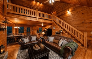 Ein Blockhaus-Interieur mit Essbereich, Wohnzimmer mit Sofa und Couchtisch sowie einer Holztreppe.