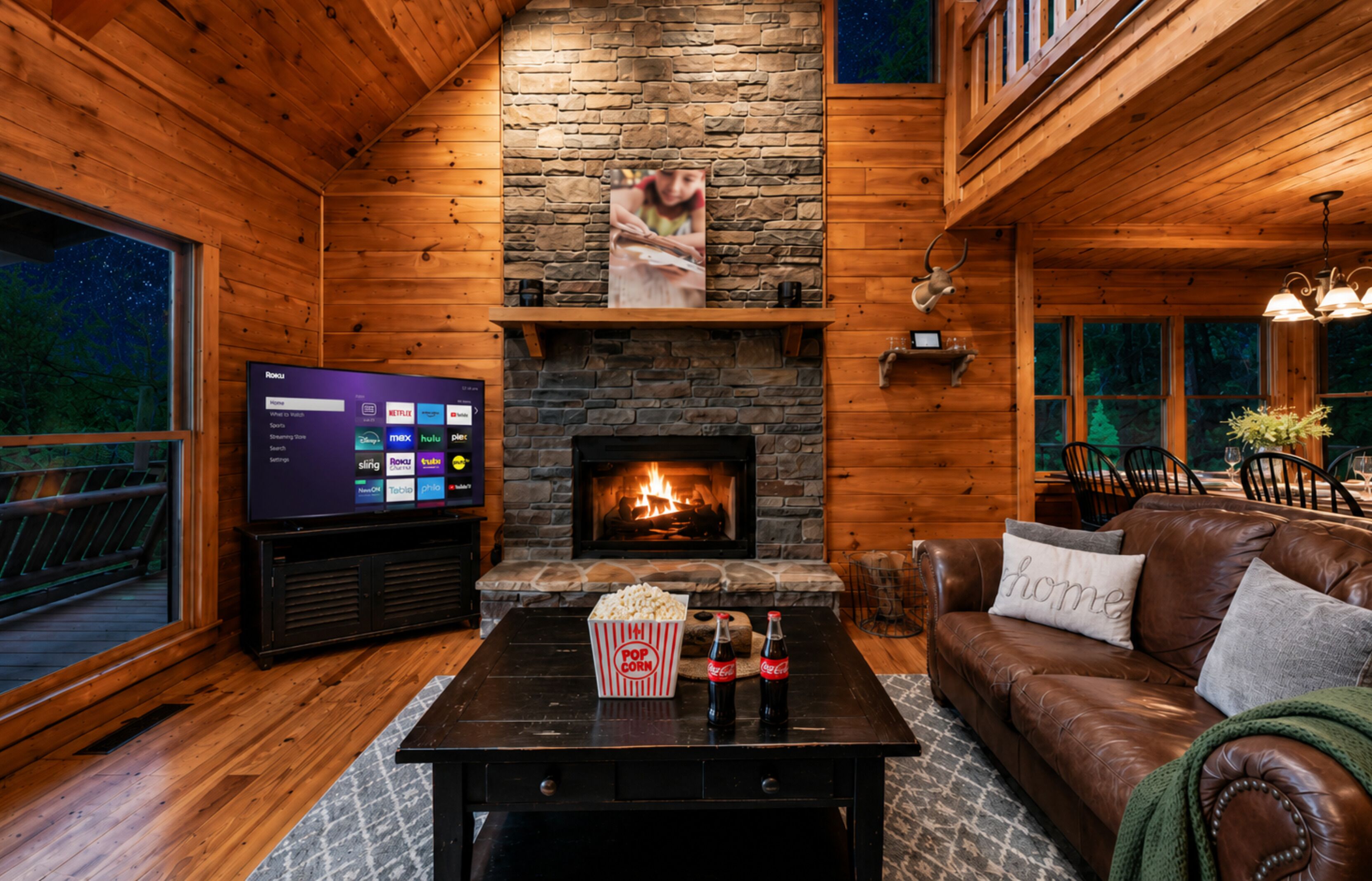 Un intérieur de chalet chaleureux avec une cheminée en pierre, un téléviseur, du pop-corn et un canapé en cuir.