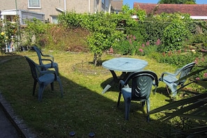 A small outdoor seating area with a round table and four chairs, surrounded by a grassy lawn and various plants. - 6 Bed House Sleeps 13 - Private Garden (Bristol)