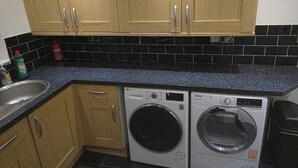 A kitchen with wooden cabinets, a black tiled backsplash, a stainless steel sink, and two front-loading washing machines. - 6 Bed House Sleeps 13 - Private Garden (Bristol)