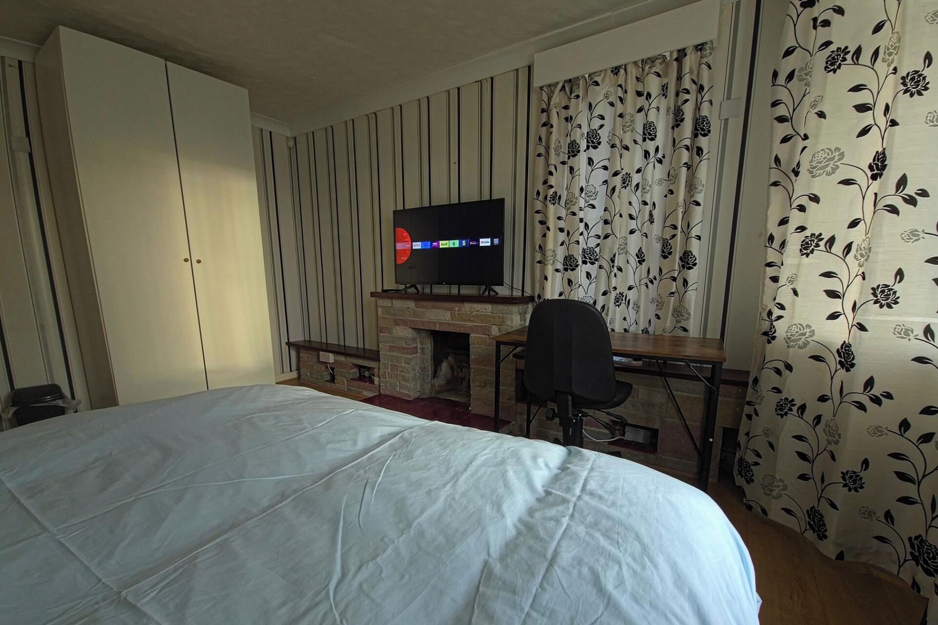 Ein Hotelzimmer mit einem Bett, einem Schreibtisch mit Computer, einem Fernseher und einem Kamin.