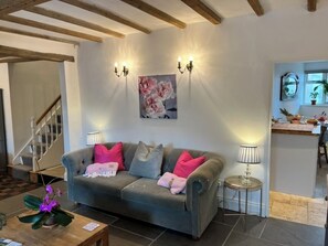 A living room with a sofa, two wall-mounted lamps, a painting, a small table with a lamp, and a staircase in the background. - Bell Cottage, a period cottage between the North Yorkshire Moors & Dales (Brompton)