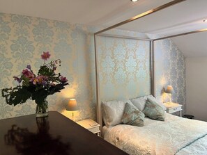 A bedroom with a bed, nightstands, a vase with flowers, and patterned wallpaper. - Bell Cottage, a period cottage between the North Yorkshire Moors & Dales (Brompton)