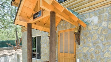 Une cabane en rondins avec un mur en pierre, une véranda en bois et une porte dotée d’une fenêtre.