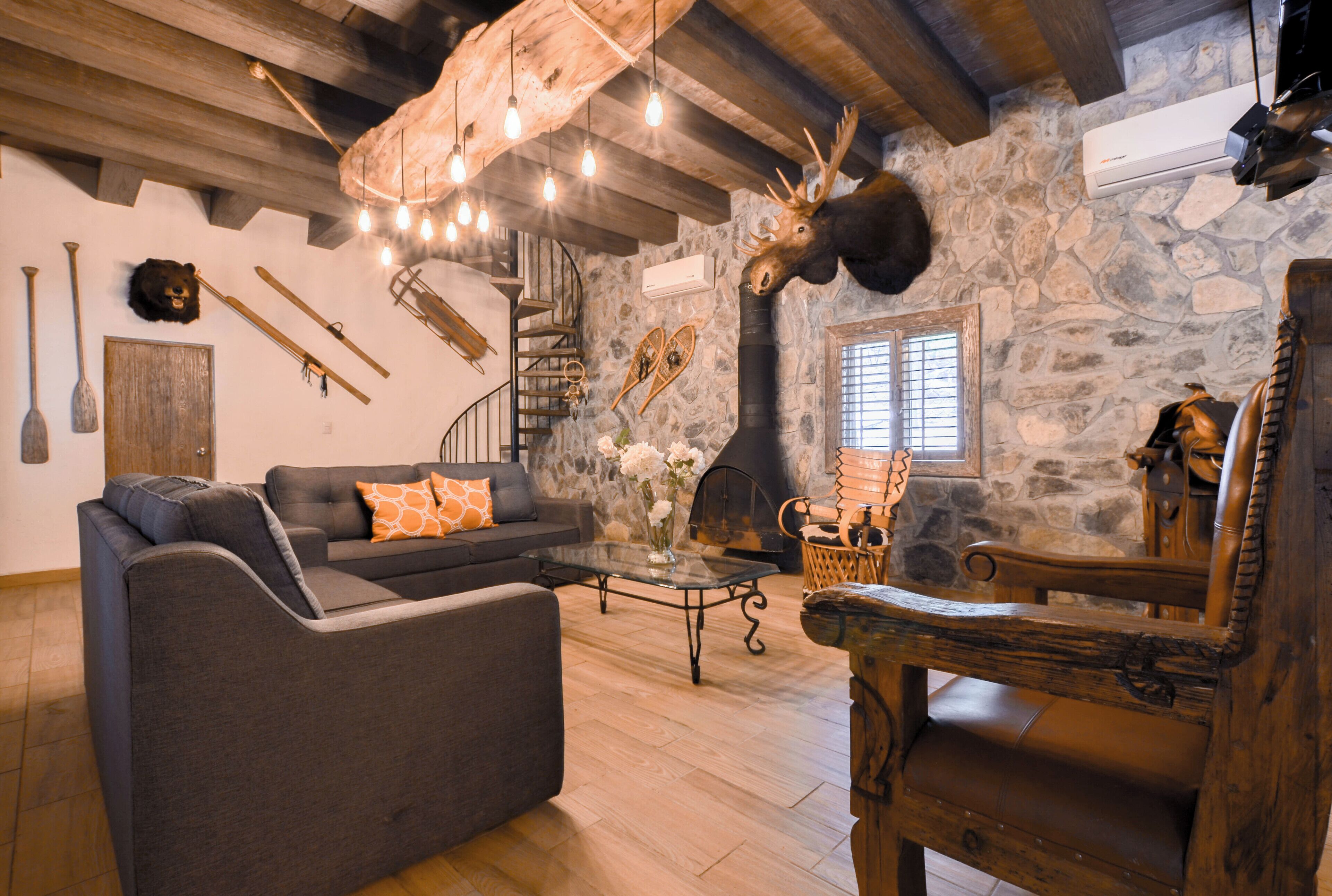 A rustic interior with a stone wall, wooden ceiling beams, a fireplace, a sofa, and a dining table.