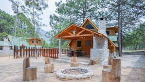 Una cabaña rústica con chimenea de piedra, terraza de madera y una fogata.