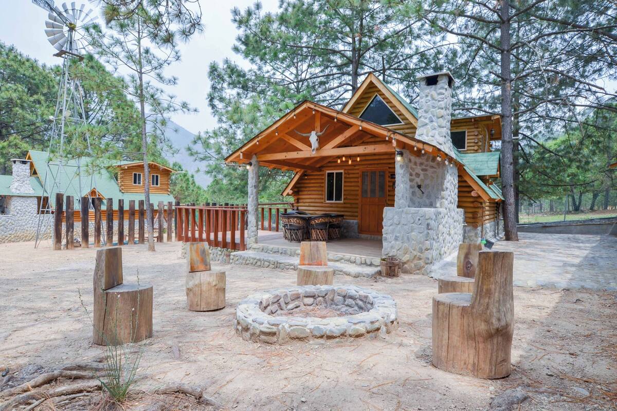 A rustic cabin with a stone chimney, wooden deck, and a fire pit.