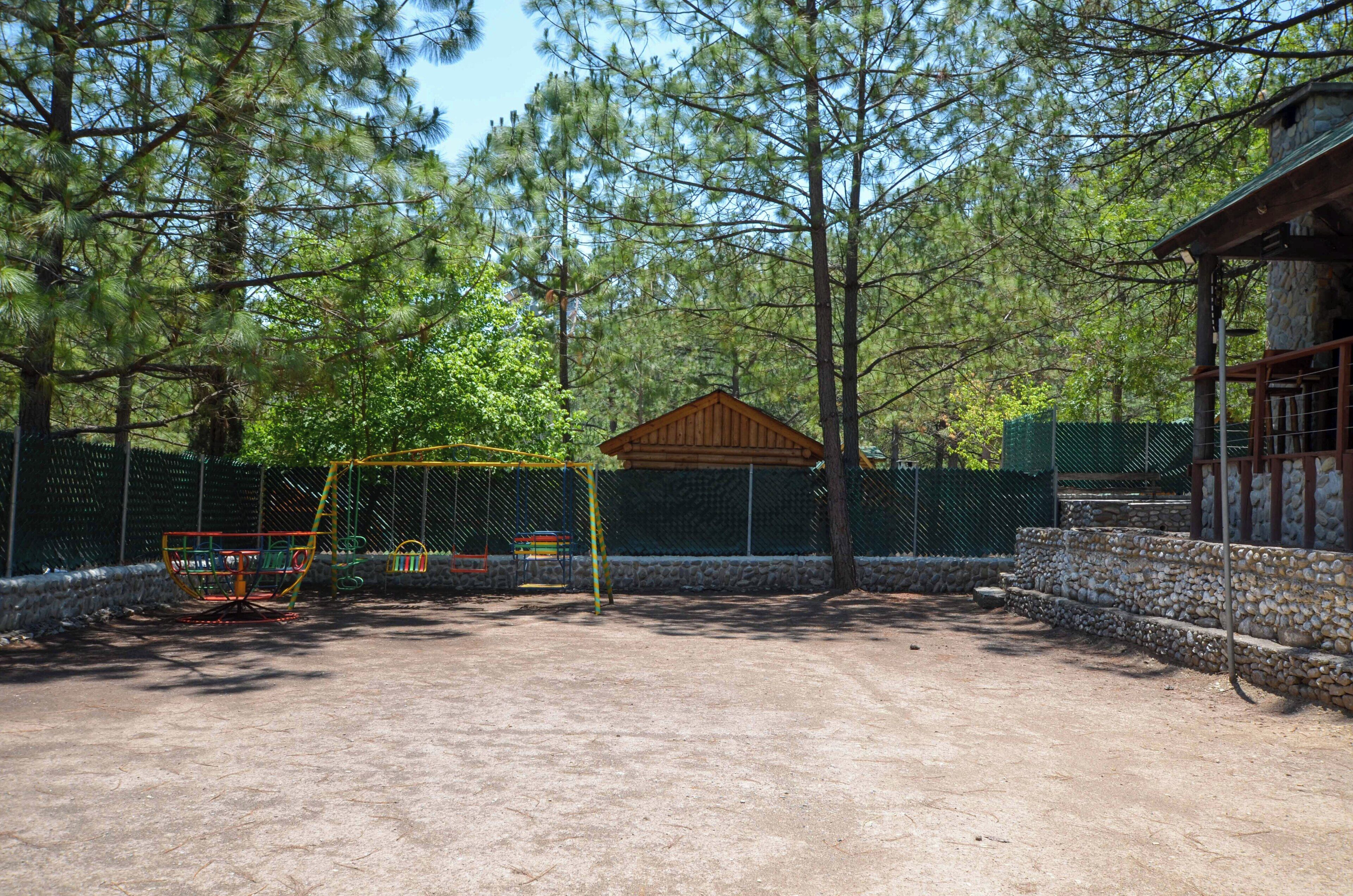 Ein von Zäunen umgebenes Außenbereich mit einer Holzhütte, möglicherweise ein Pavillon, umgeben von Bäumen.