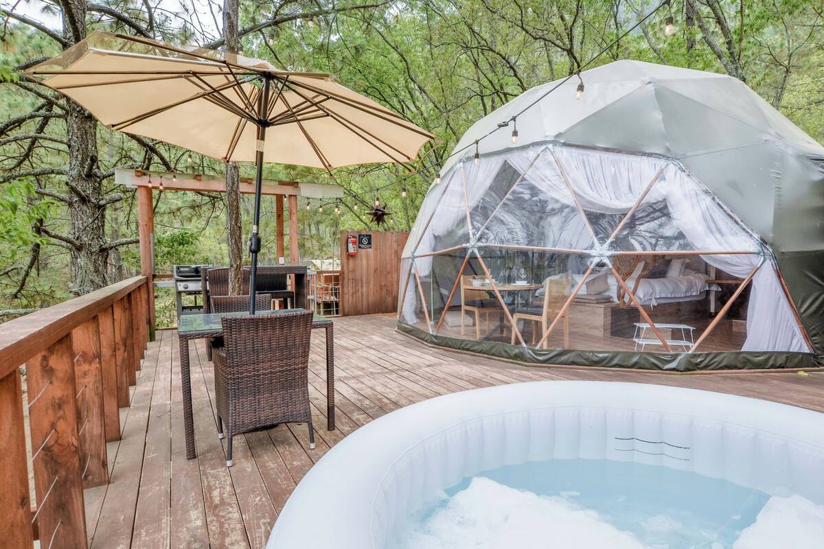 A wooden deck with a hot tub, a covered seating area, and a geodesic dome tent.
