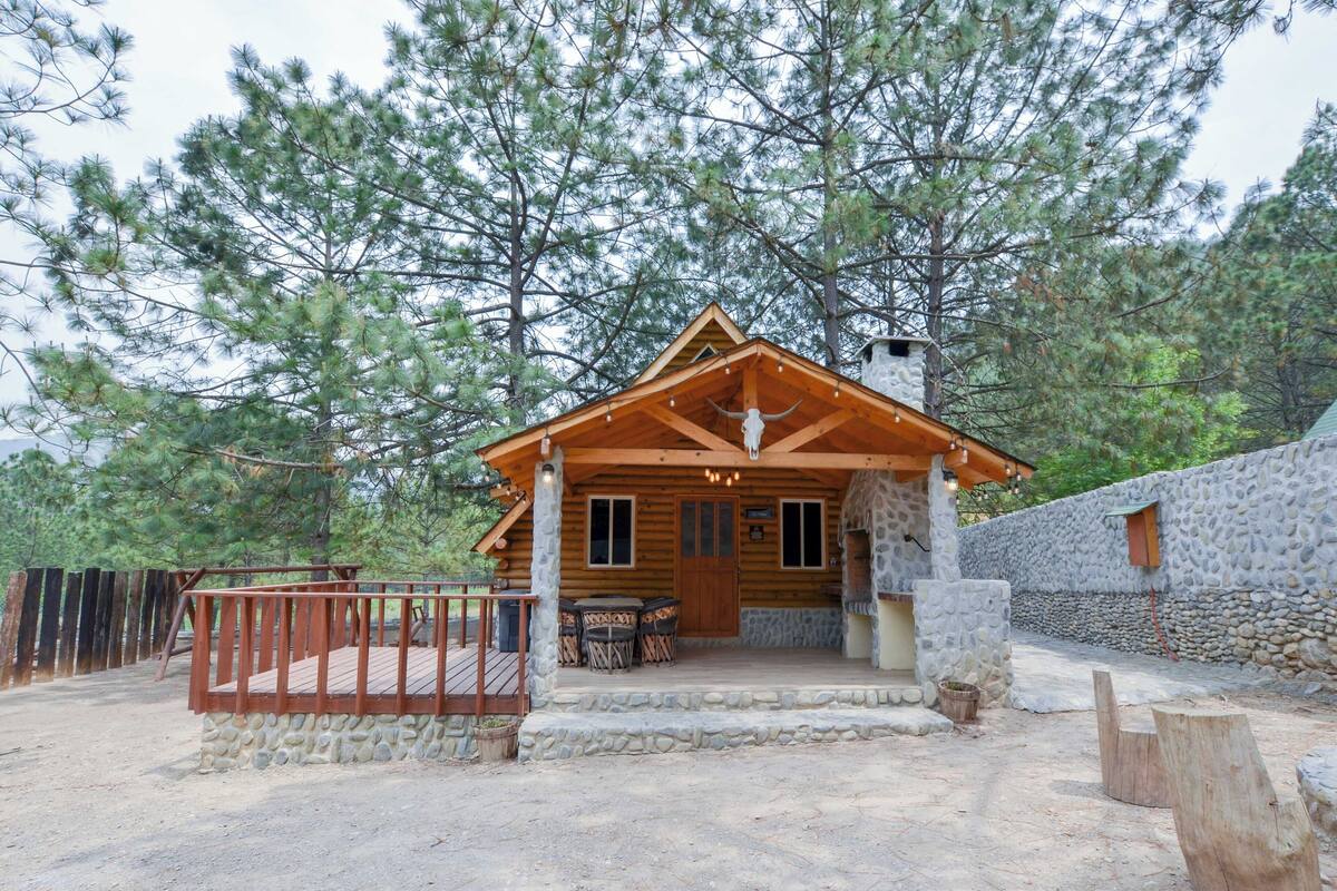 A rustic cabin with a stone wall, wooden deck, and a porch with outdoor seating.