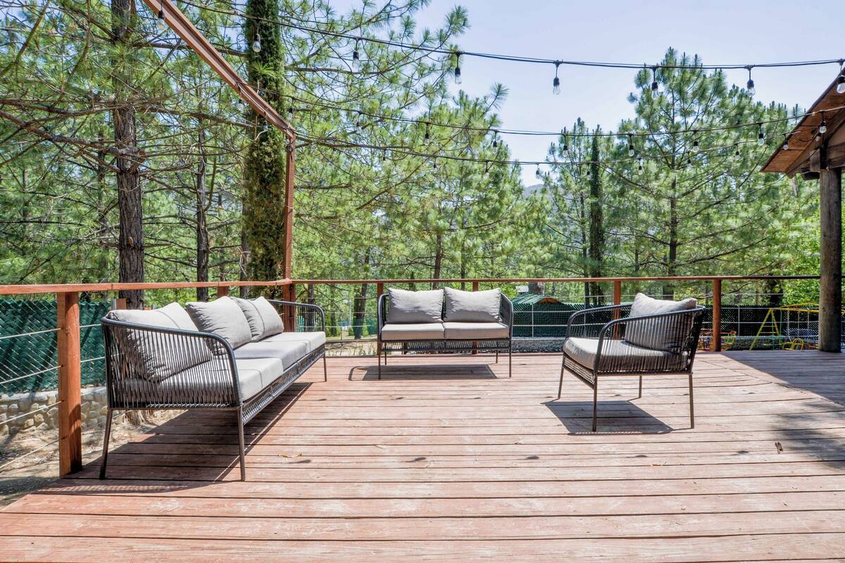 A wooden deck with two sofas and a table, surrounded by a wooden fence and trees.