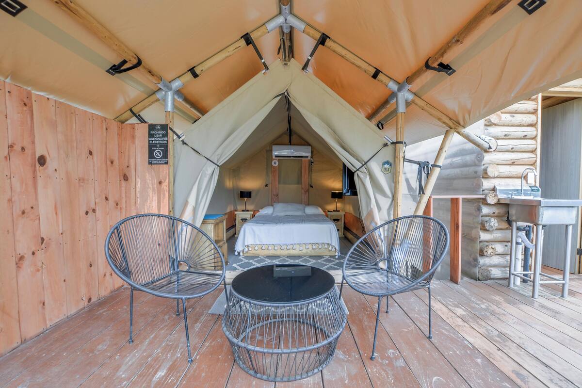 A tented accommodation with a bed, two chairs, a table, and a sink.