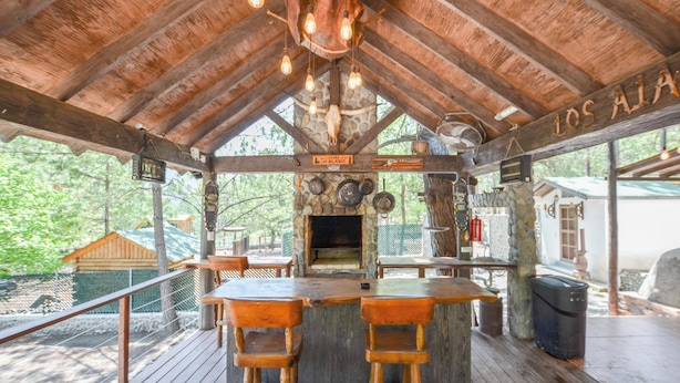 Ein rustikaler Barbereich aus Holz mit Kamin aus Stein, hölzernen Barhocker und einem Schild mit der Aufschrift 'Los Alamos'.