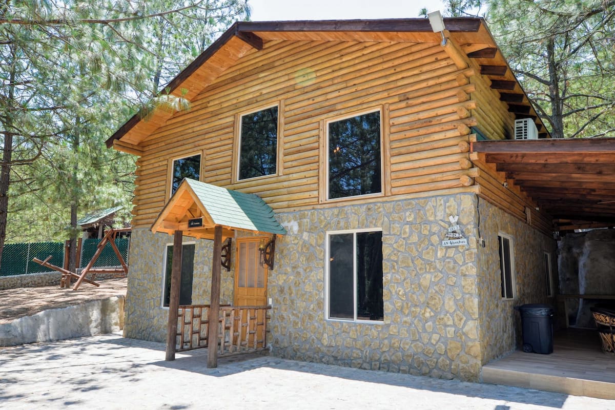 A log cabin with a stone facade, a porch, and a small attached structure.