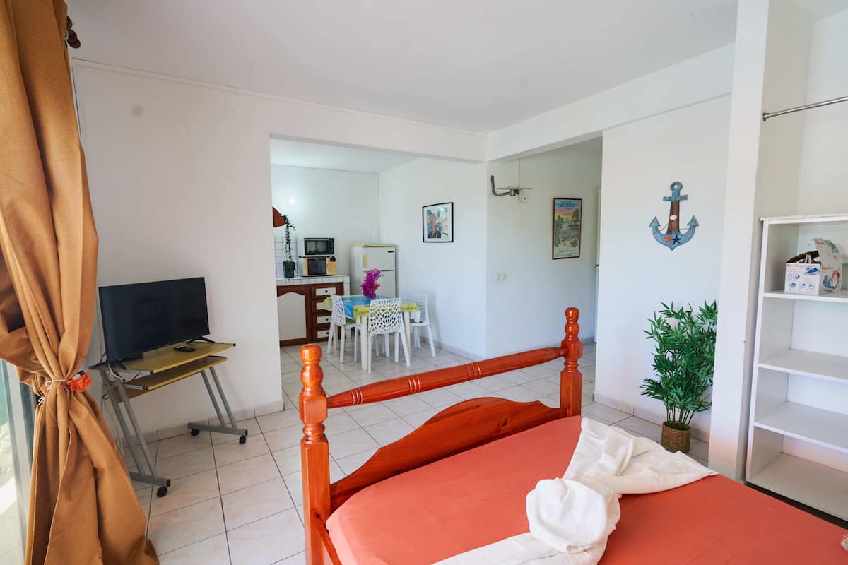 A bedroom with a wooden bed, a television on a stand, a small table with chairs, and a white wall with a framed picture and an anchor decoration.
