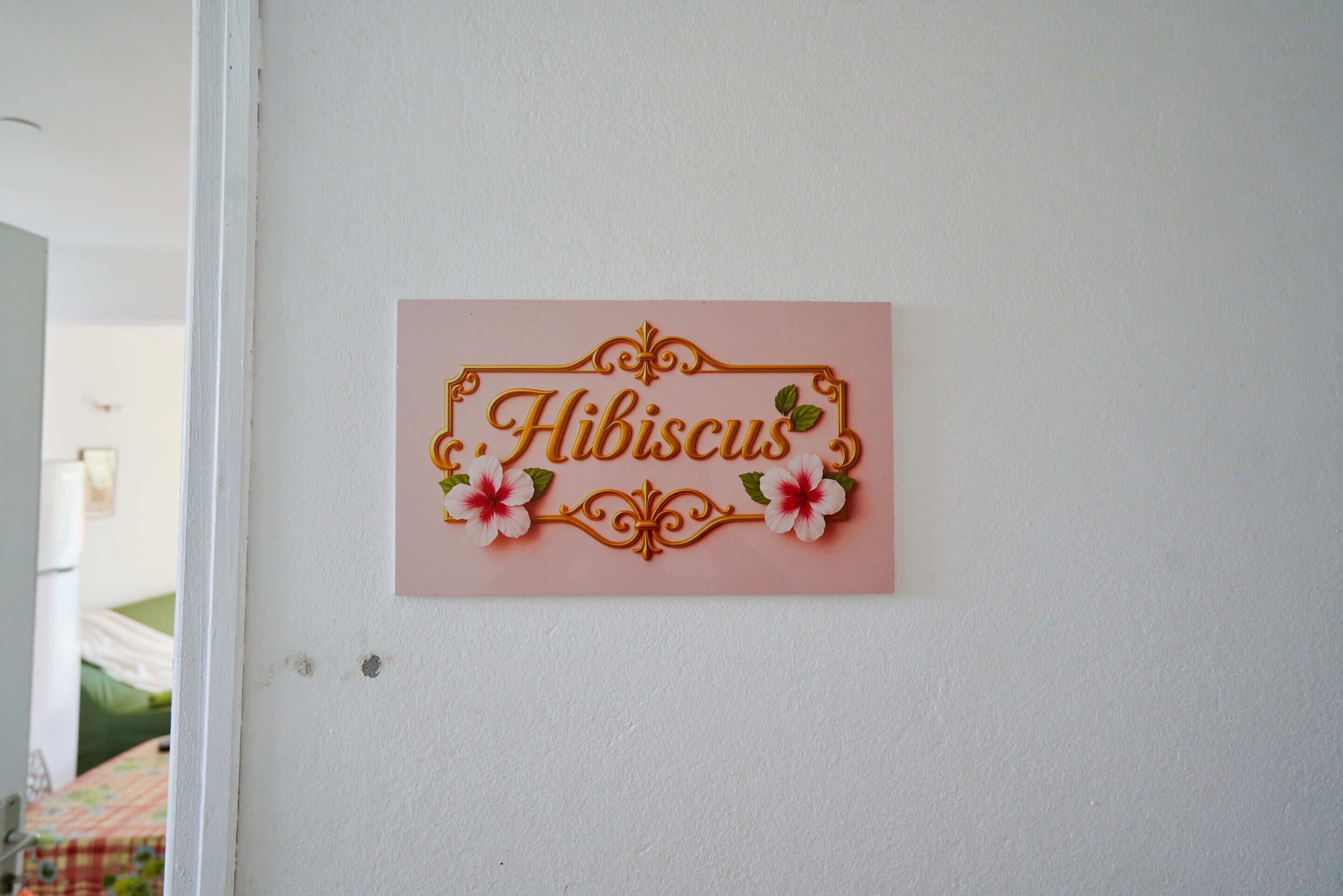 Un letrero en la pared con el nombre 'Hibiscus' rodeado de detalles decorativos.