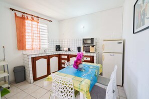A compact kitchen with a microwave, refrigerator, and a dining area with a table and chairs. - RESIDENCE LE LAGON (Sainte-Anne)