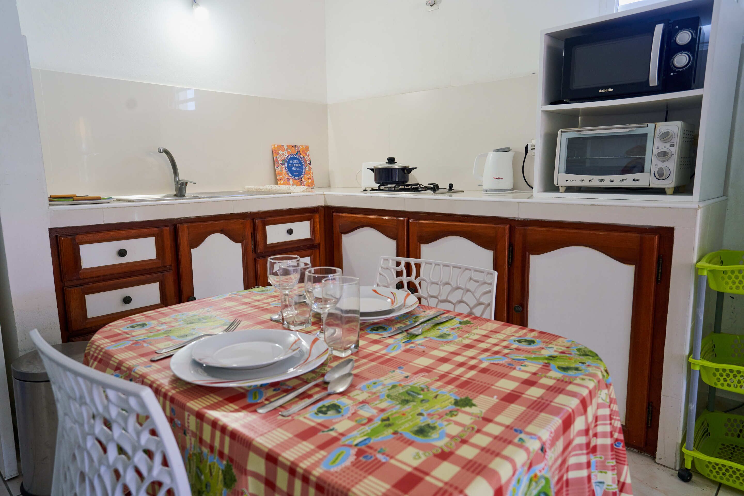 Cucina con forno a microonde, tostapane e lavello. Un tavolo da pranzo con piatti, posate e bicchieri.