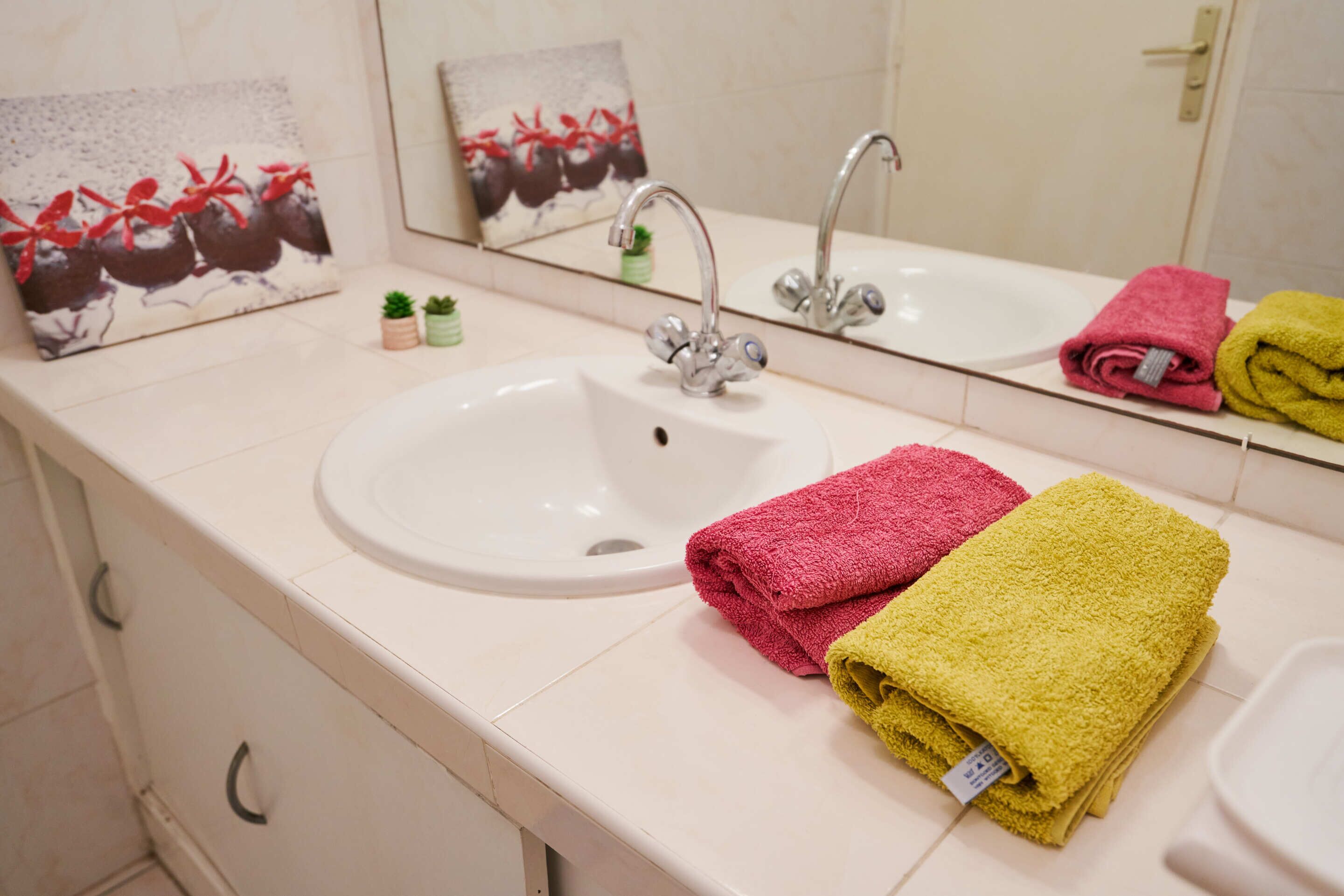 Een badkamer met een witte wastafel, een spiegel en twee handdoeken (één roze en één geel) op het aanrecht.