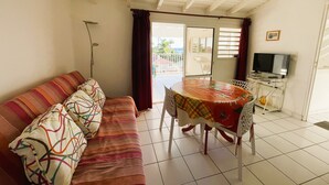 Uma sala de estar com sofá, mesa de jantar com cadeiras, televisão e varanda com vista.