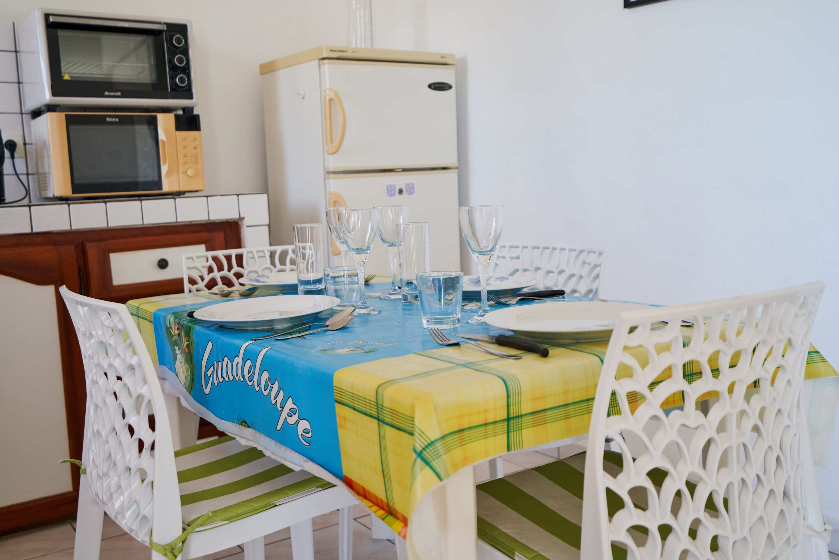 A dining area with a table set for four, chairs, a microwave, and a refrigerator.