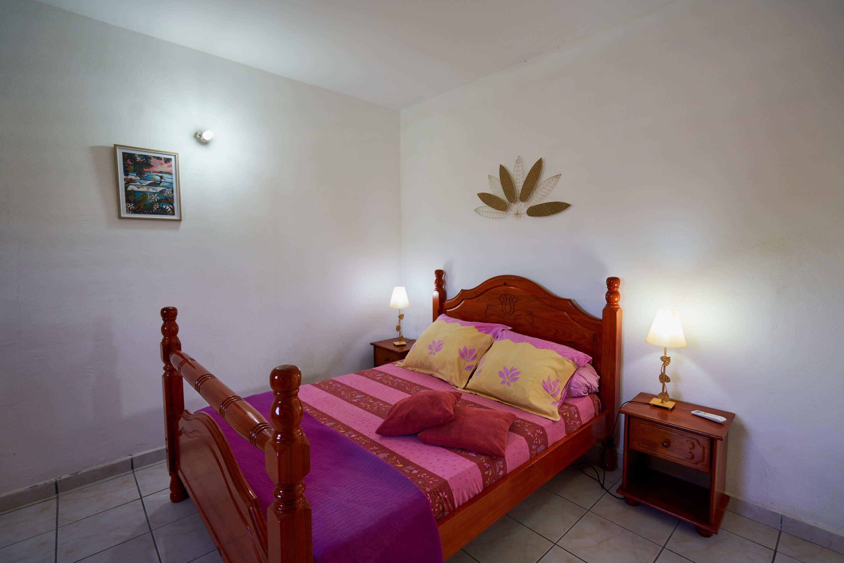 A single bed with a wooden headboard, two bedside tables with lamps, a wall-mounted flower decoration, and a framed picture on the wall.