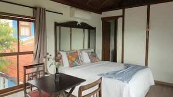 A room with a bed, a table, chairs, a window, and a thatched roof.