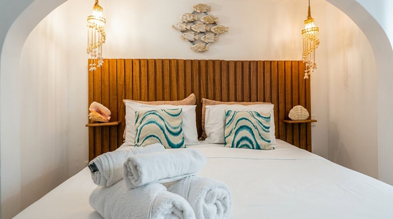 Una cama con cabecera de madera, dos mesitas de noche con adornos, y una lámpara de pared.
