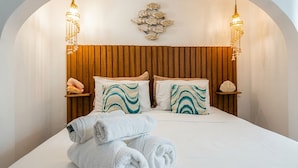 Una cama con cabecera de madera, dos mesitas de noche con adornos, y una lámpara de pared.